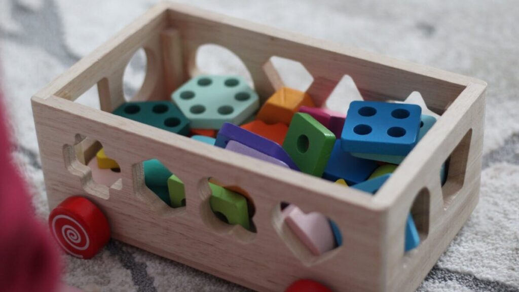 Espaço de brincar seguro e estimulante em casa com brinquedos educativos organizados em caixa de madeira colorida.